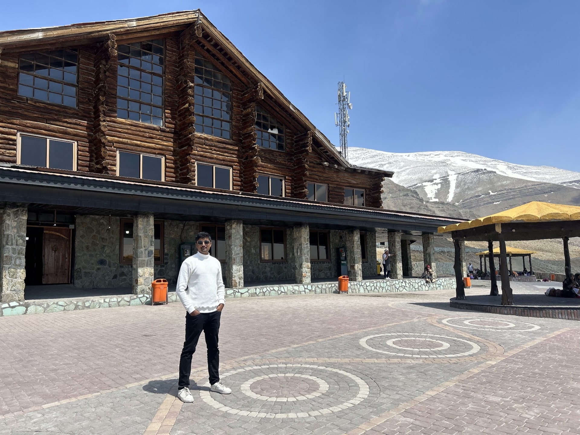 Vasanth outside a mountain lodge beneath snowy peaks